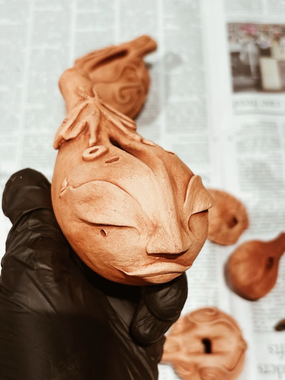 A sculpted terracotta incense holder held in a gloved hand, fresh from the worktable
