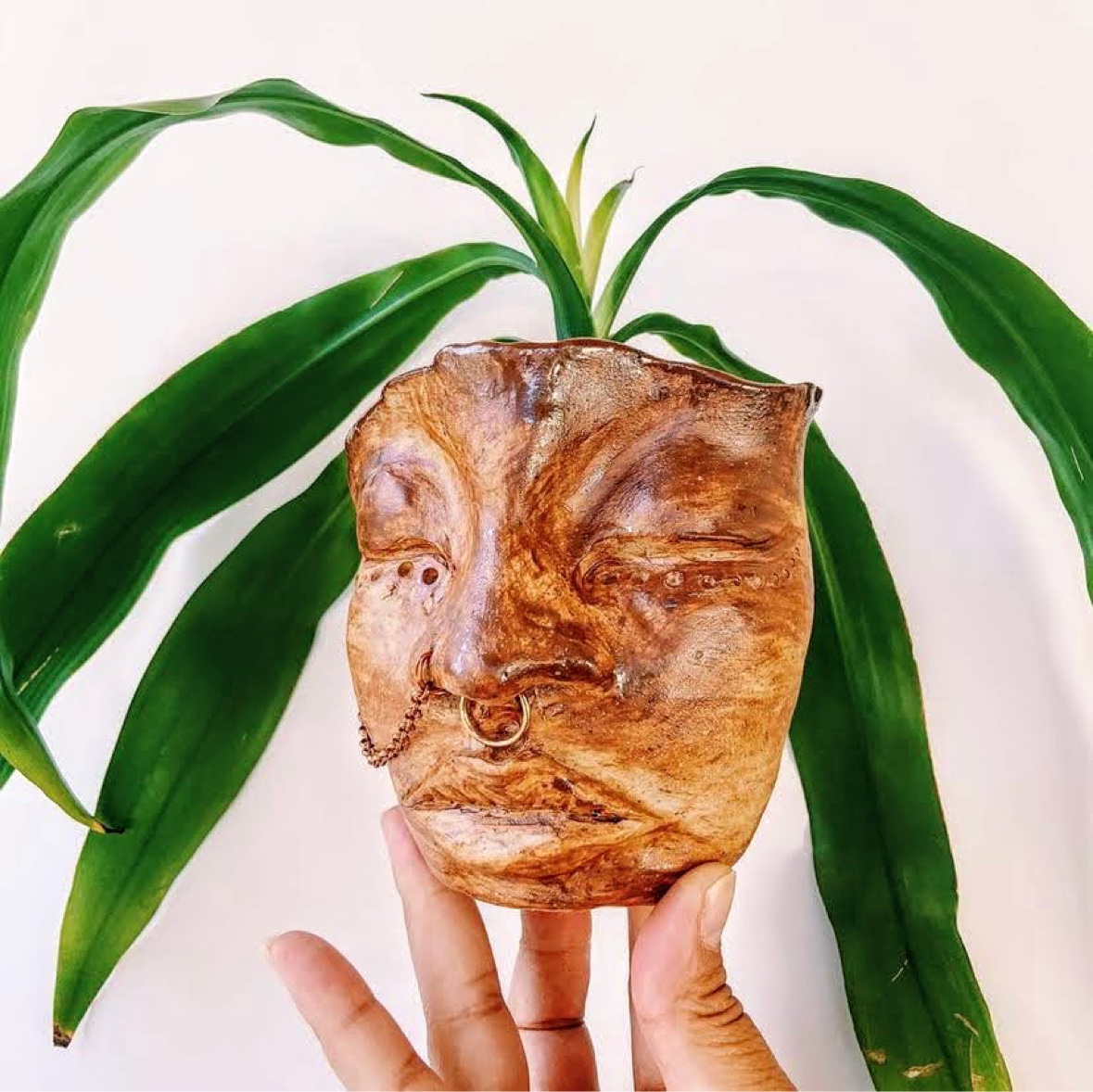 A sculpted face planter pot with green leaves in warm golden-brown clay