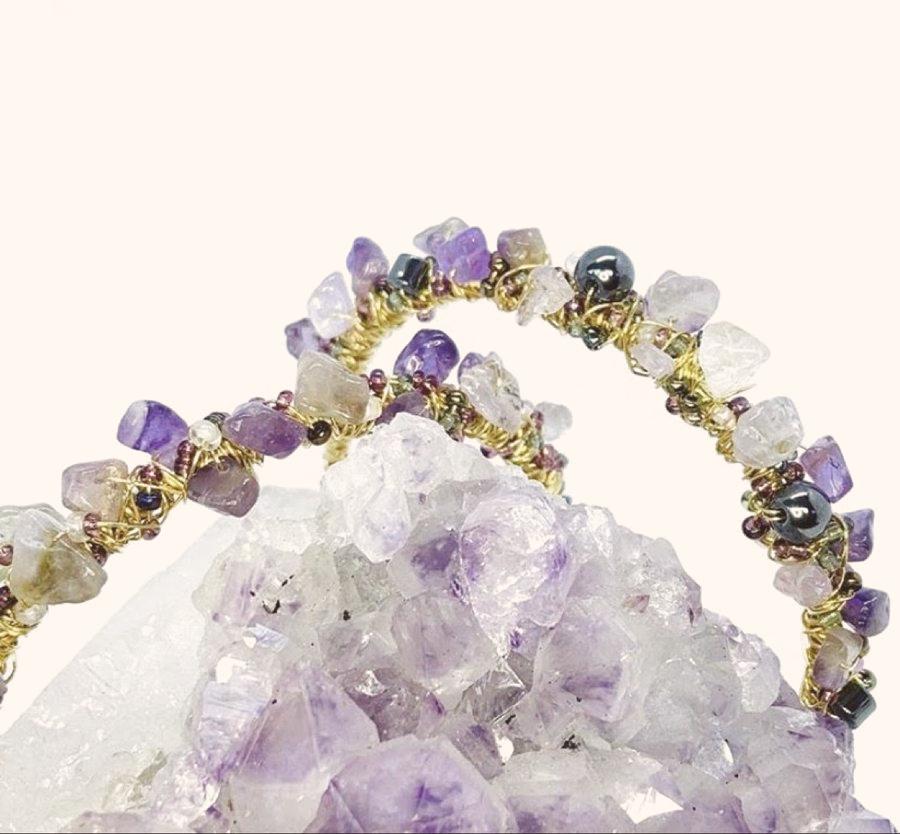 A wire-wrapped amethyst bracelet resting on a white crystal cluster