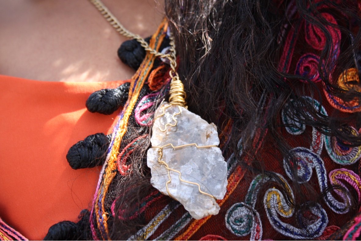 Close-up of a wire-wrapped quartz pendant on a gold chain, resting against colorful embroidered fabric