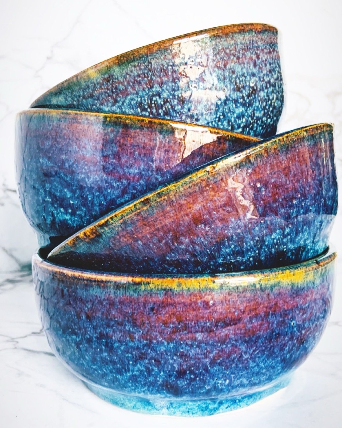 A stack of glazed stoneware bowls in deep blue and violet galaxy glaze