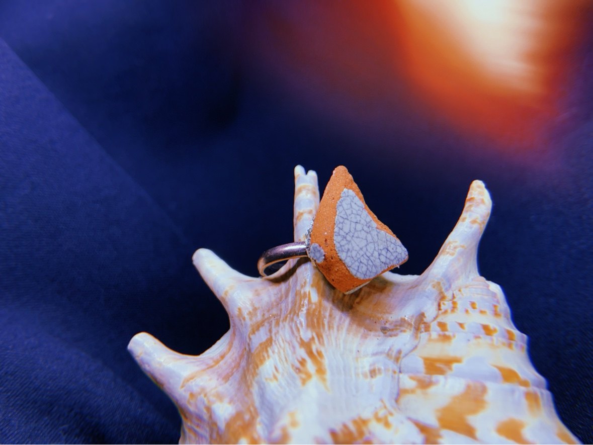 A sculpted clay ring resting on a spotted shell