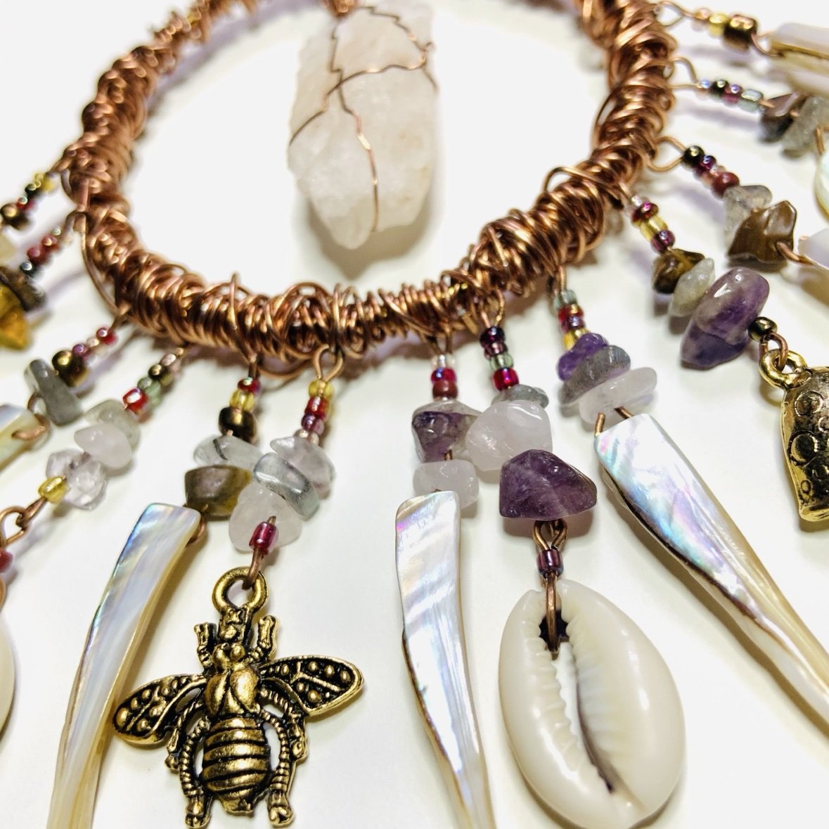 A copper wire-wrapped statement necklace with amethyst, shell, cowrie, and bee charms