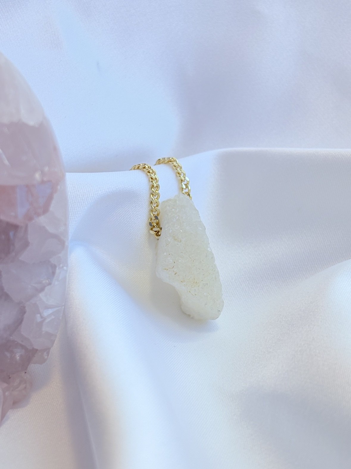 A raw white druzy quartz pendant on a gold chain