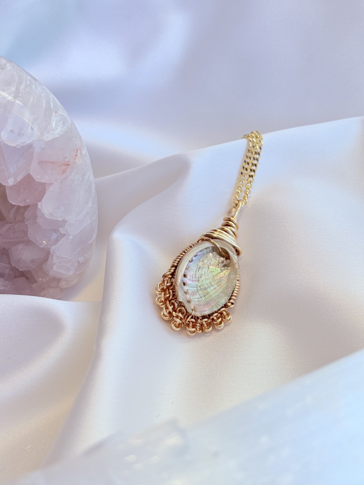 A wire-wrapped abalone shell pendant on a gold chain