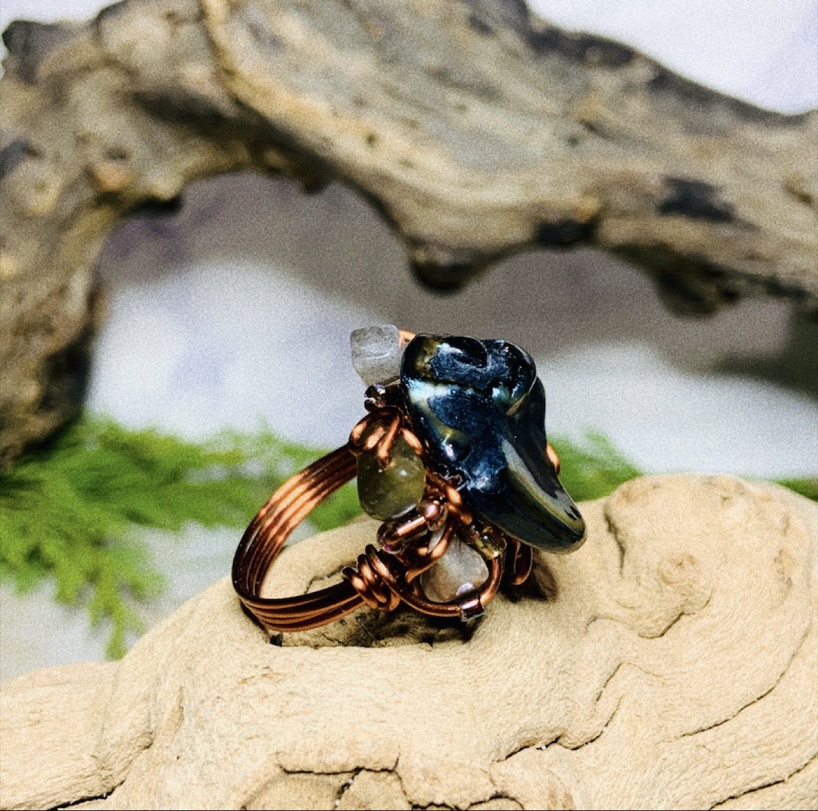 A wire-wrapped abalone ring with copper wirework on driftwood