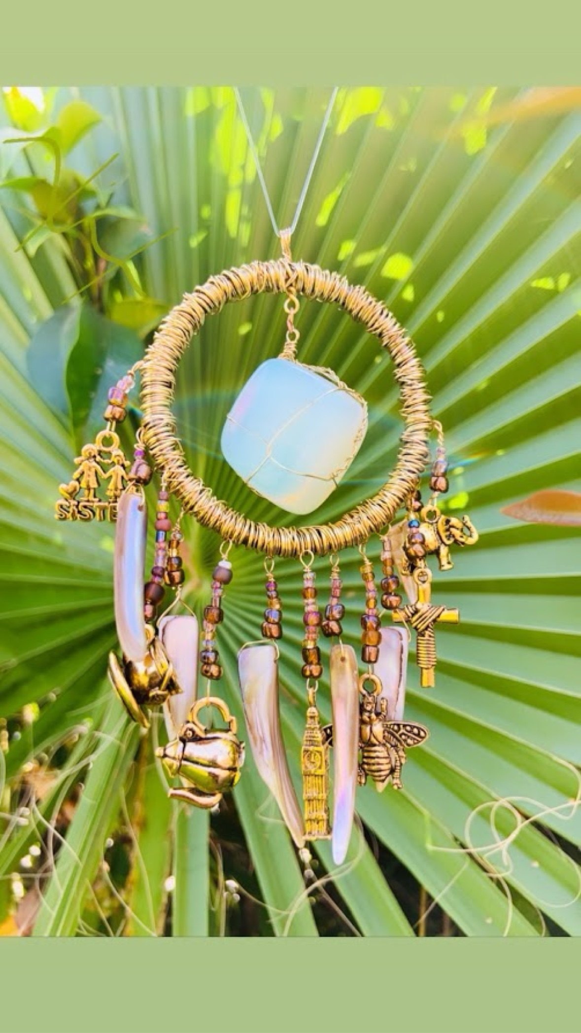 A wire-wrapped suncatcher with charms, shells, and an opalite stone hanging outdoors