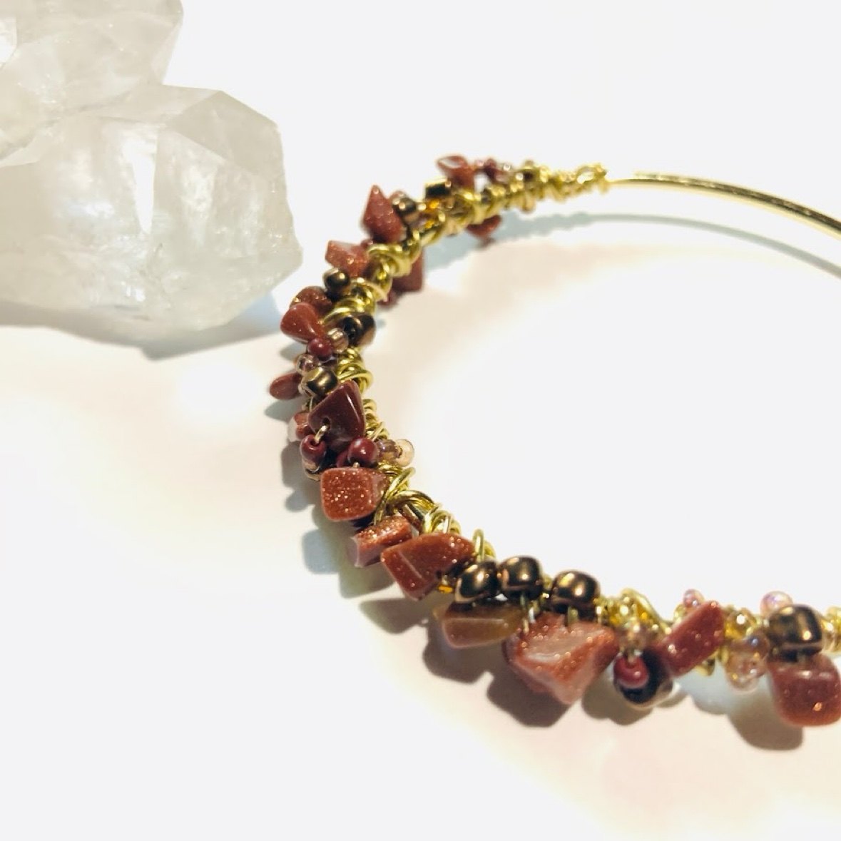 A gold bangle wrapped with goldstone chips and bronze beads