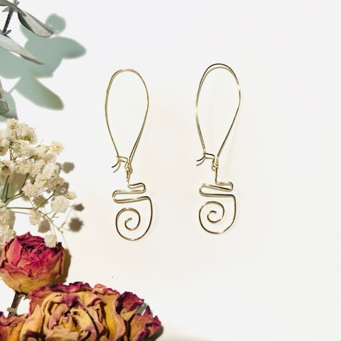 Gold spiral drop earrings photographed with dried roses