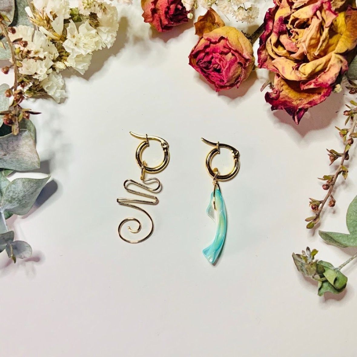 Mismatched gold huggie earrings — a wire spiral and a shell drop — with dried roses