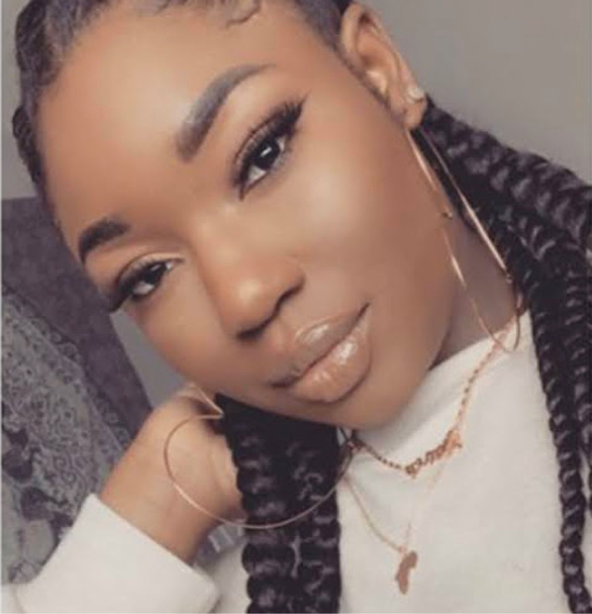 A woman wearing gold hoop earrings and a gold Africa-pendant necklace