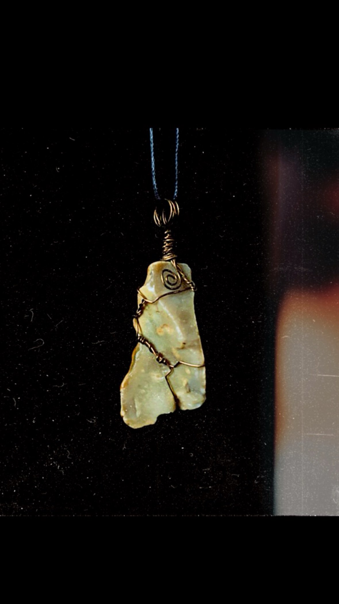 A wire-wrapped raw stone pendant photographed on black
