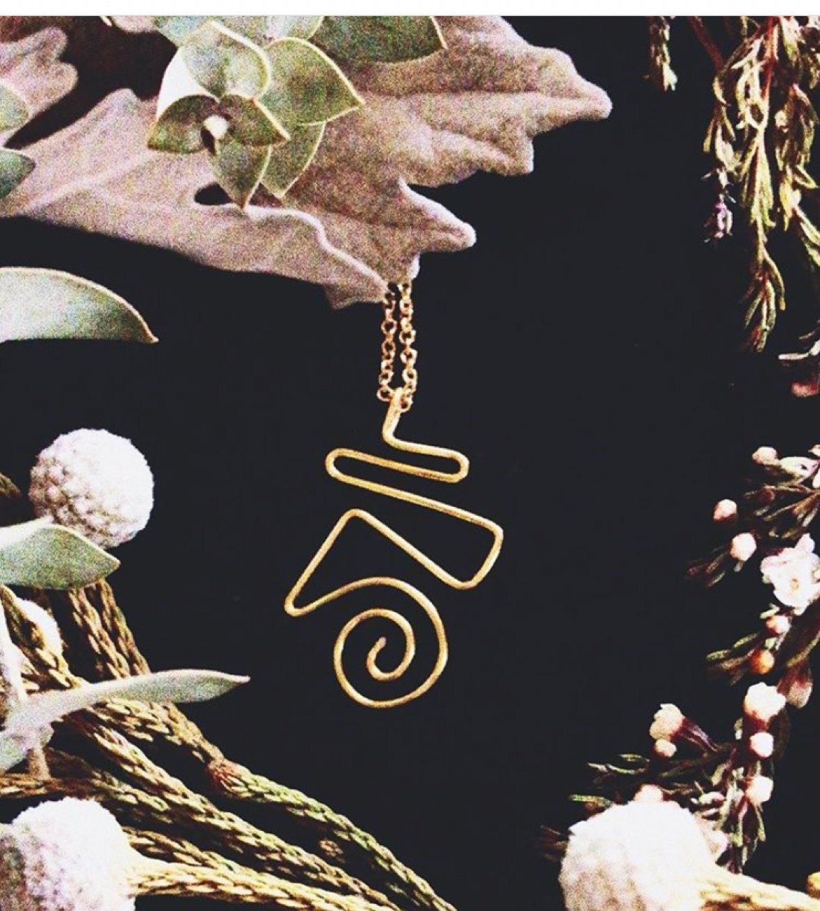 A gold wire serpent necklace hanging among dried botanicals