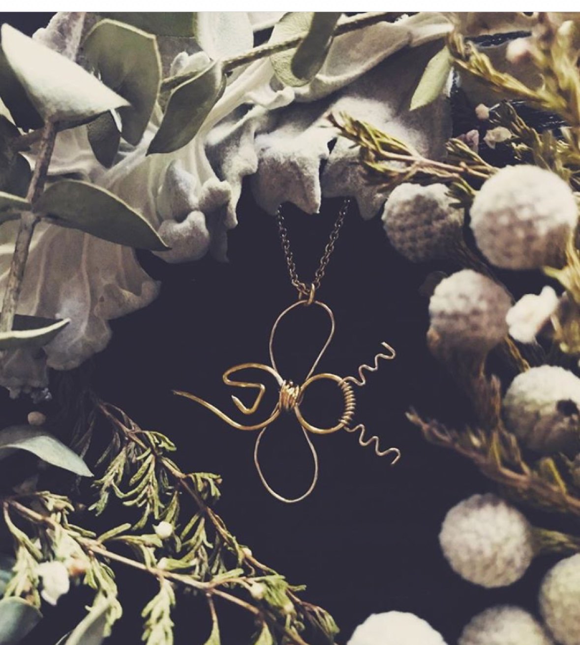 A gold wire bee pendant necklace among dried botanicals