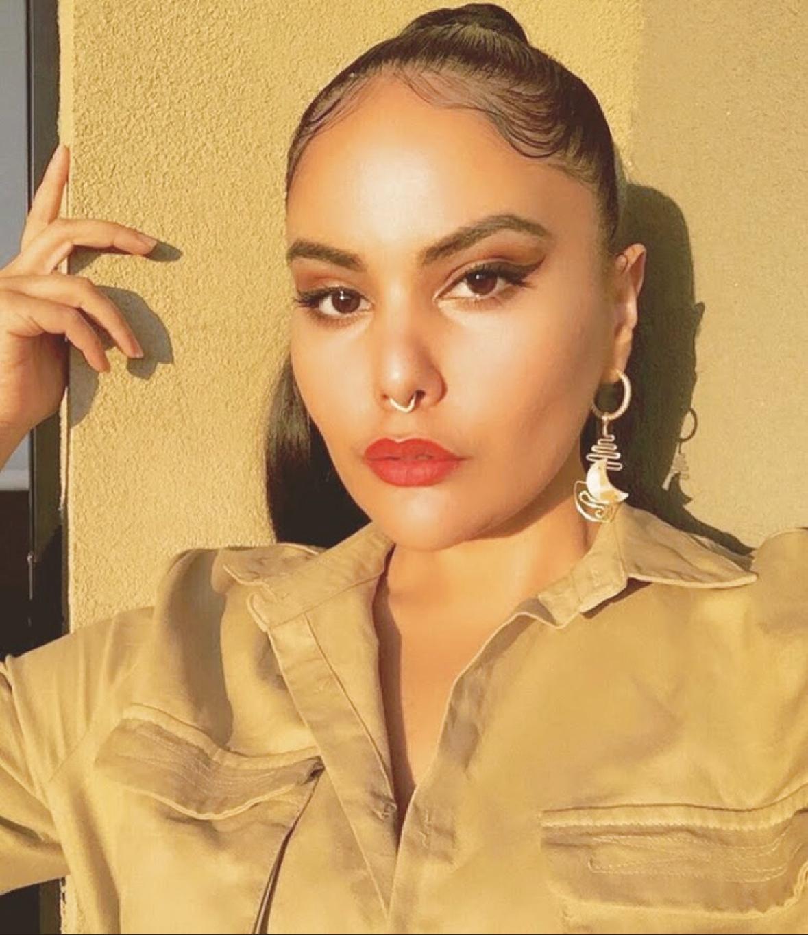 A person wearing sculptural wire spiral earrings against a warm wall in golden hour light