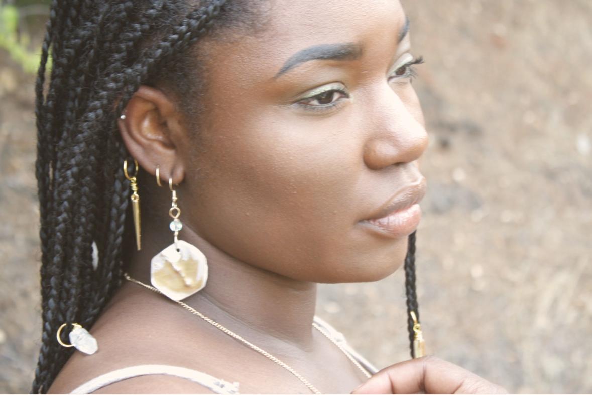 A person with long braids wearing a large sunstone clay earring outdoors