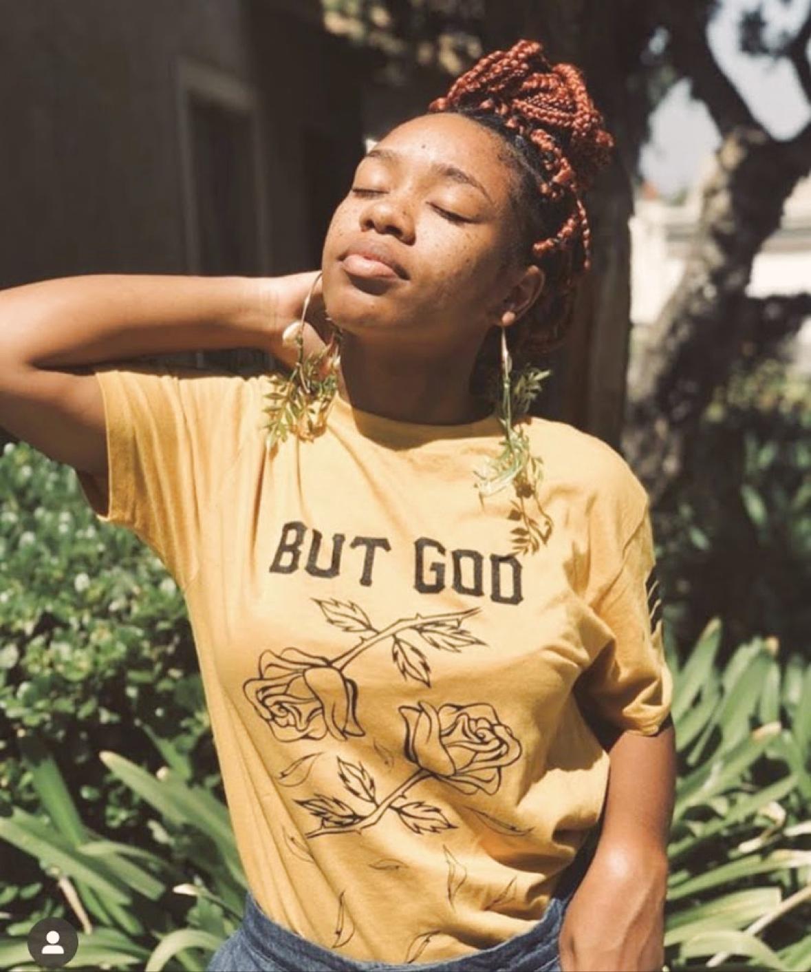 A person in golden sunlight wearing long hand-shaped leaf earrings with a mustard top