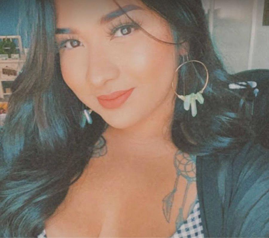 A person with long dark hair wearing large petal hook earrings
