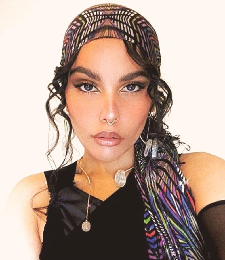 A person in a patterned headwrap wearing a wire-wrapped stone pendant