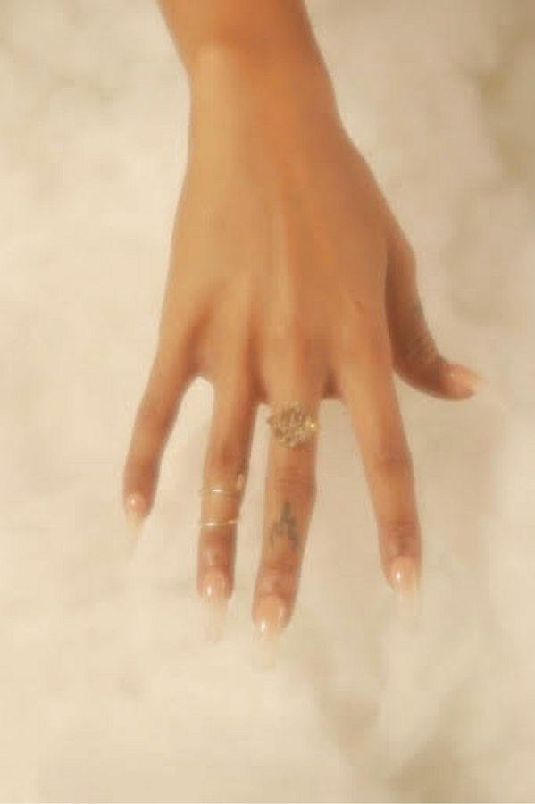 A hand wearing a crystal cluster ring and thin bands over pale fabric